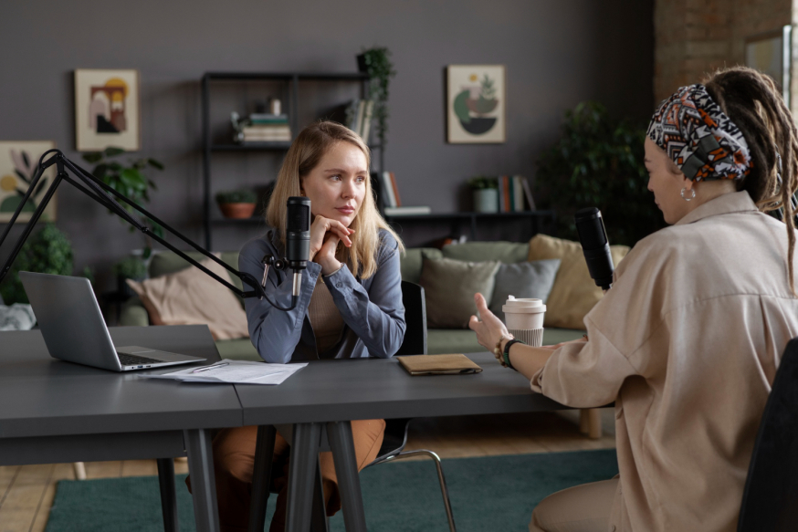 Afbeelding: Twee vrouwen voeren een gesprek voor een podcast-opname in een professioneel ingerichte kantoorruimte