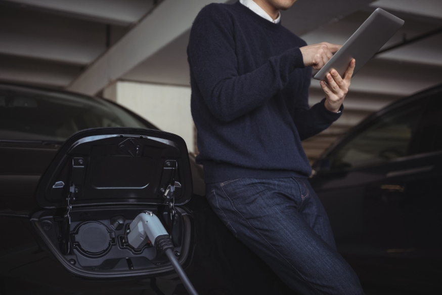 Waarom elektrisch rijden in 2026 een zakelijke prestatiekeuze is Afbeelding: Zakelijke rijder gebruikt een tablet naast een elektrische auto die wordt opgeladen