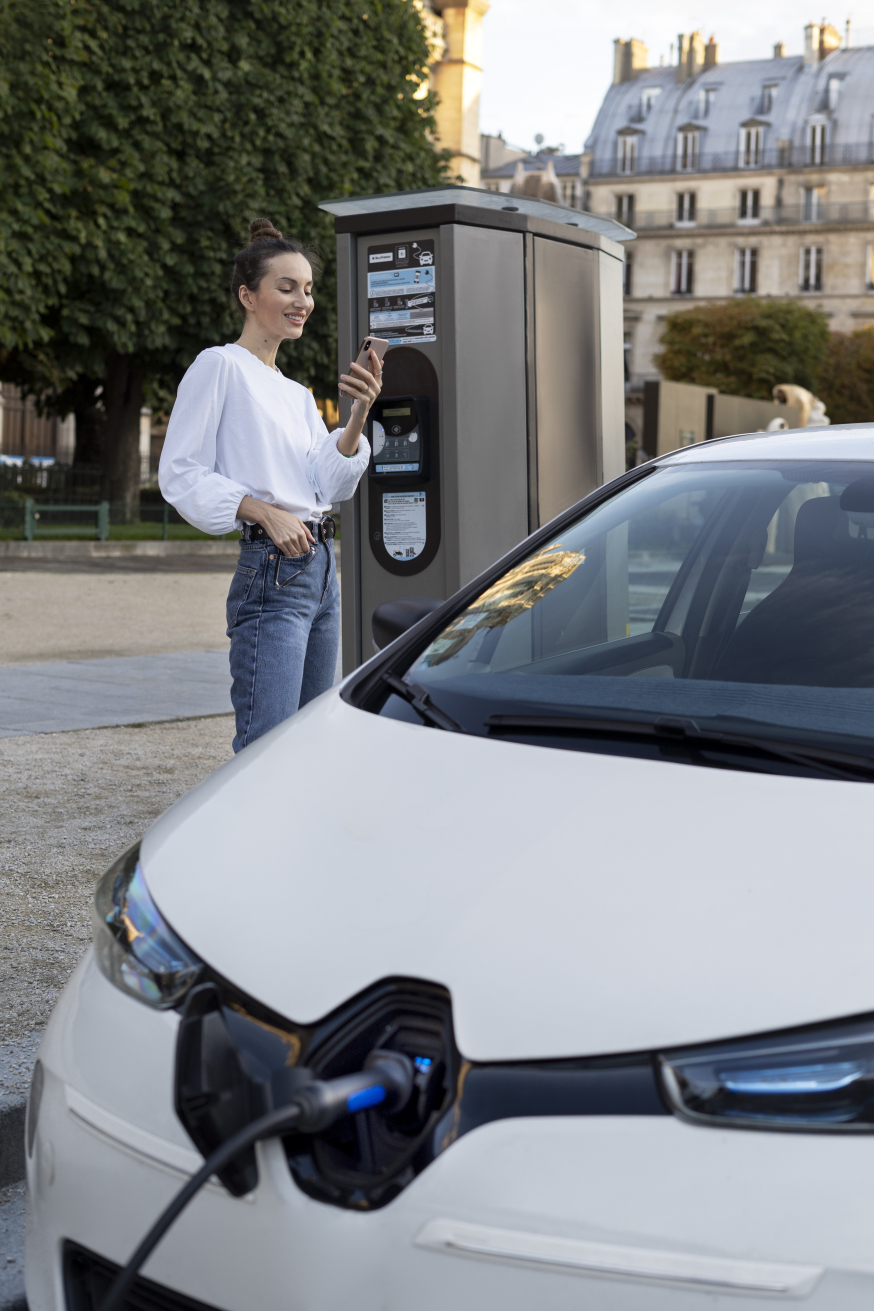 Waarom elektrisch rijden in 2026 een zakelijke prestatiekeuze is Afbeelding: Bestuurder staat met smartphone bij een openbare laadpaal naast een elektrische auto