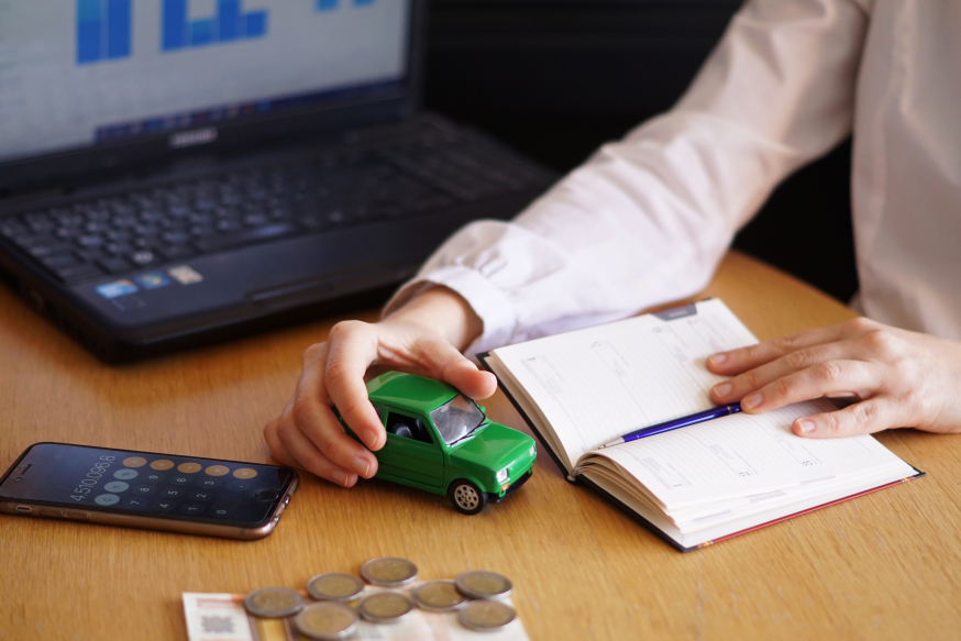 Waarom elektrisch rijden in 2026 een zakelijke prestatiekeuze is Afbeelding: Persoon berekent autokosten van elektrisch rijden met een modelauto, calculator, munten en notitieboek op tafel