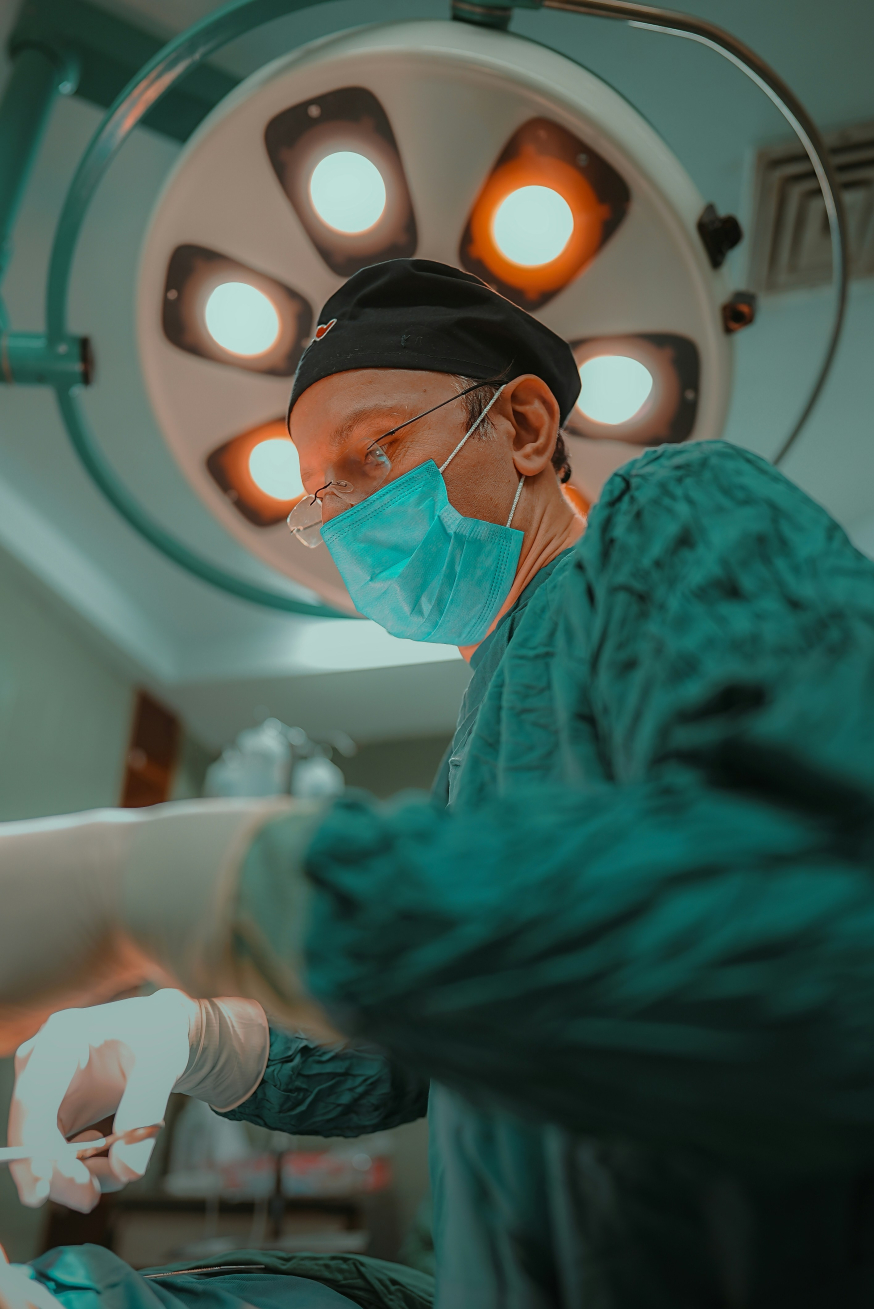 Een chirurg in groene operatiekleding en met mondkapje aan het werk onder een felle operatielamp