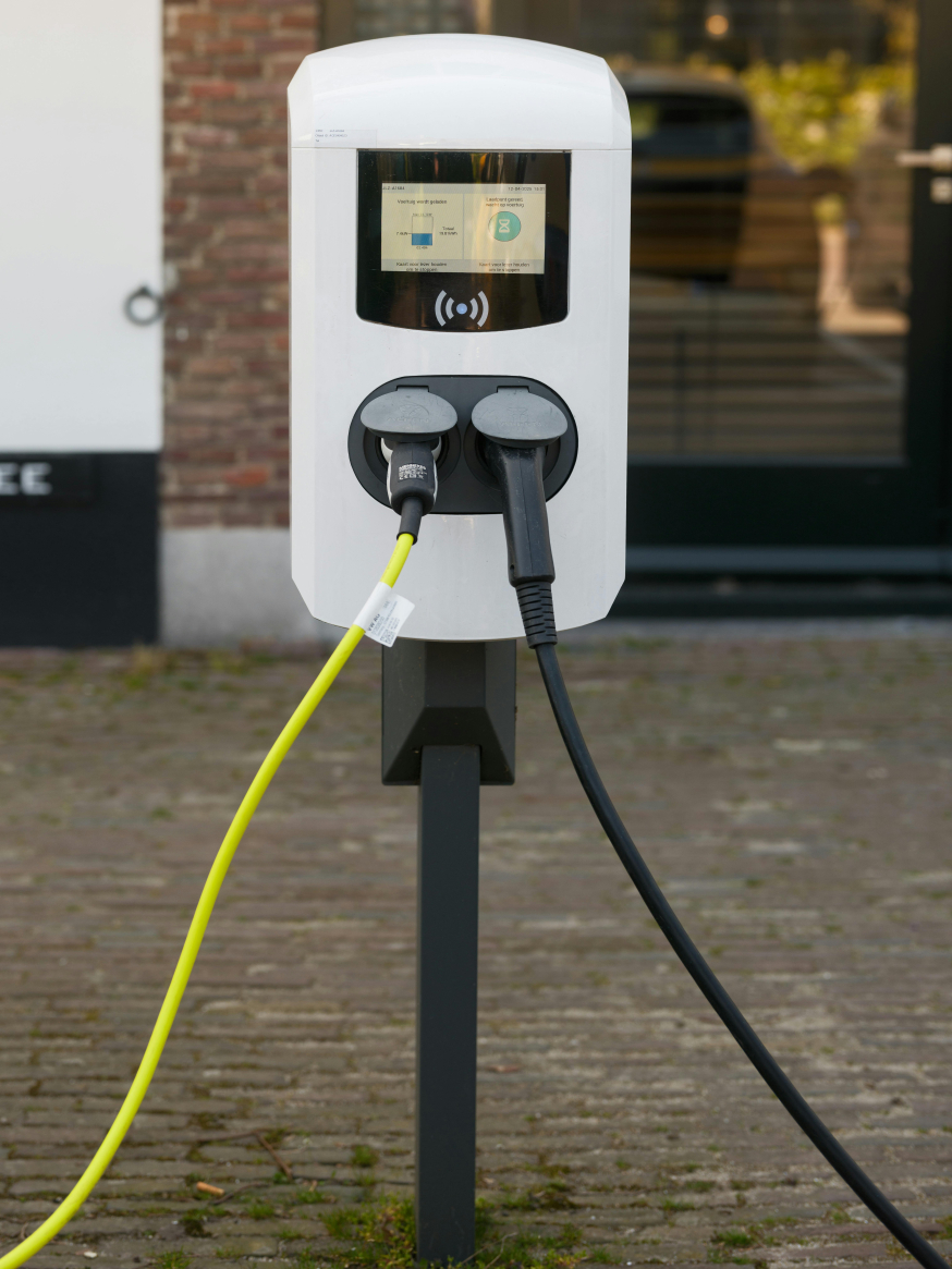 Waarom elektrisch rijden in 2026 een zakelijke prestatiekeuze is Afbeelding: Close-up van een laadpaal met twee aangesloten laadkabels bij een gebouw